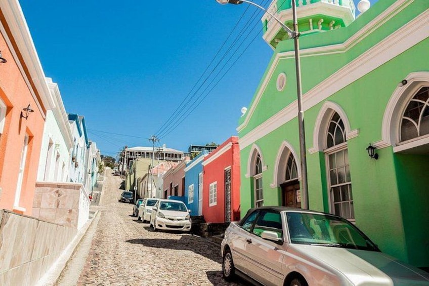 A cobblestone street lined with colorful buildings, parked cars, and a clear blue sky. 4