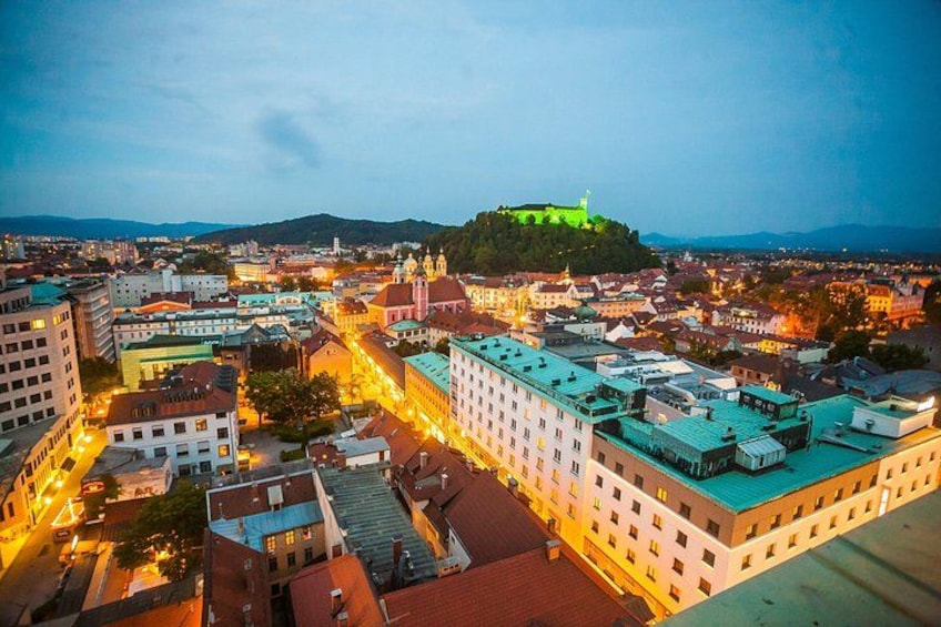 A cityscape with a prominent hilltop castle, illuminated buildings, and a river. 2