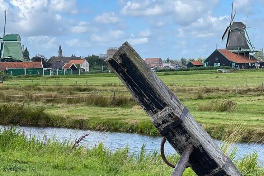 En vindmølle, et træpæl, en flod og huse i et landligt landskab. 5