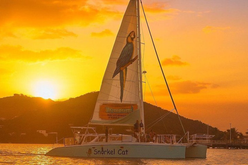 A sailboat named 'Snorkel Cat' with a bird design on its sail, sailing on water with a sunset in the background. 2