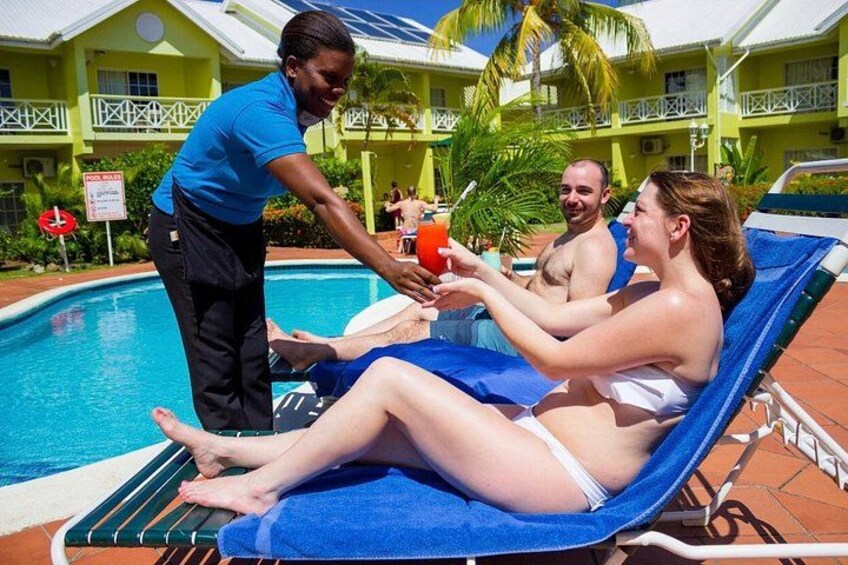 Szenenbild am Pool mit einer Person, die zwei entspannten Personen auf Liegen ein Getränk serviert. 2