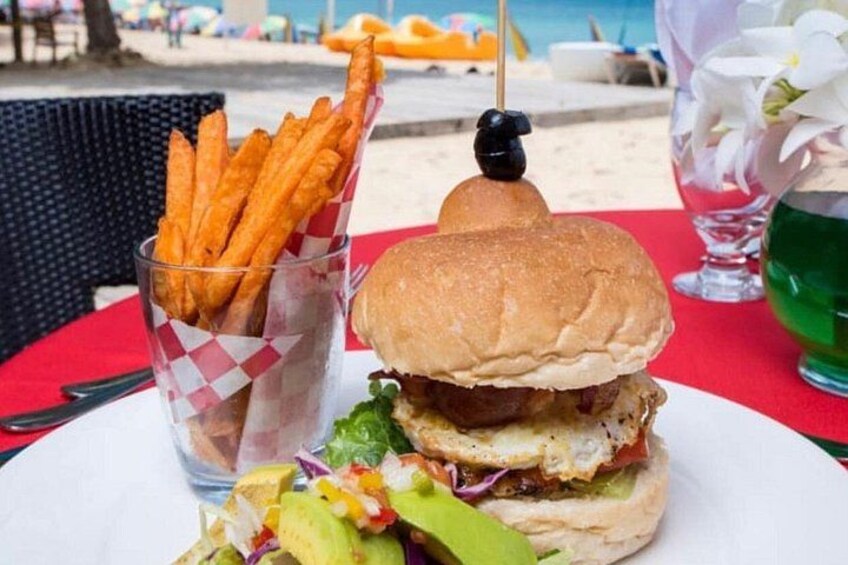 Ein Burger mit Pommes und einem Getränk, im Hintergrund ein Strand. 3