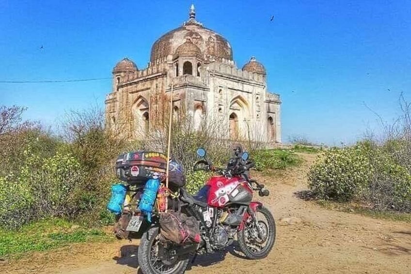 A motorcycle parked on a dirt path with a large, historic building in the background. 4