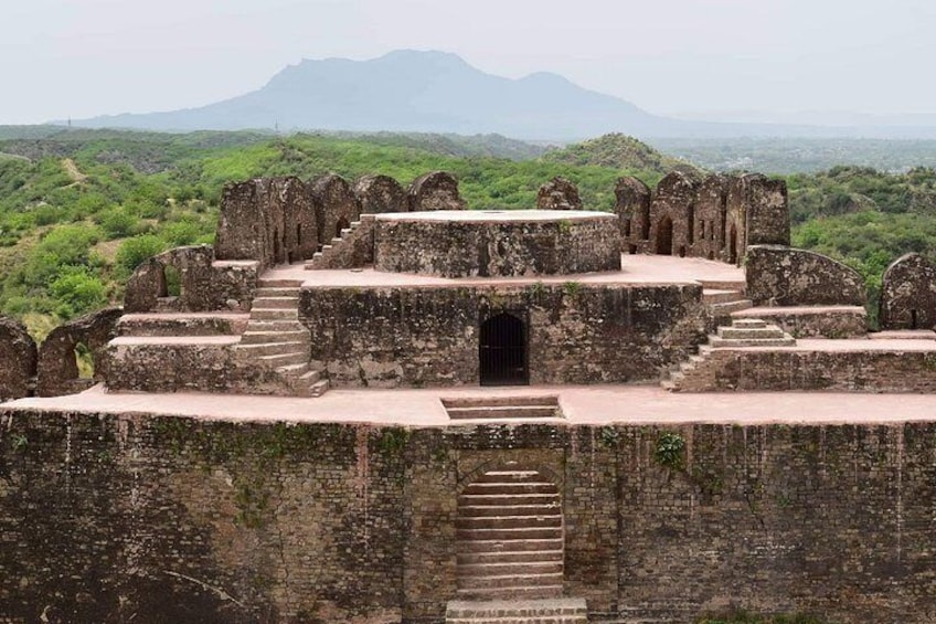 An ancient fort with a central staircase leading to a gate, surrounded by lush greenery and mountains in the background. 5