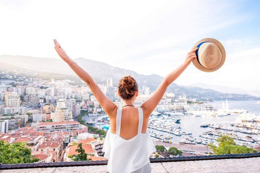 A person with arms raised, holding a hat, overlooking a cityscape with buildings and a body of water. 1