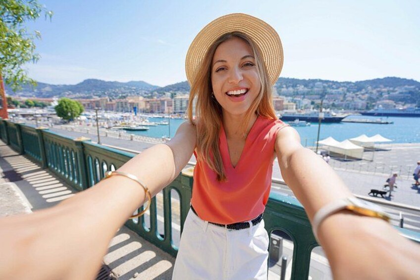 A person taking a selfie with a scenic harbor and mountains in the background. 3