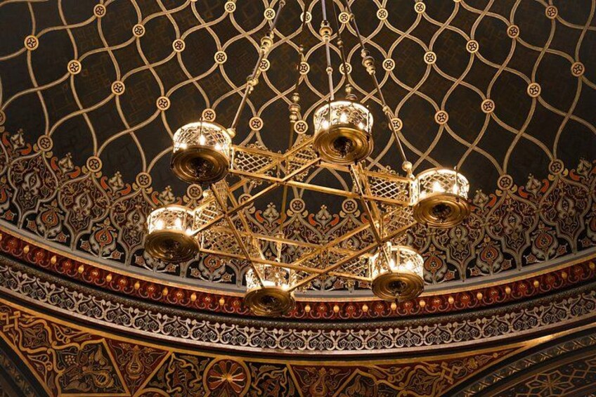 Un candelabro ornamentado con múltiples luces, patrones intrincados en el techo y detallados adornos en las paredes. 2