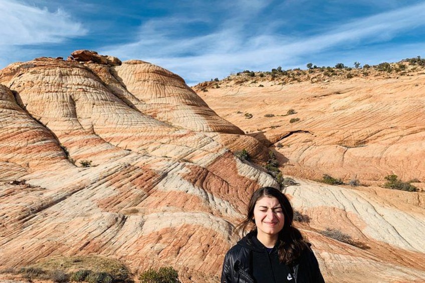 A person standing in front of a large rock formation with layered sedimentary patterns. 2