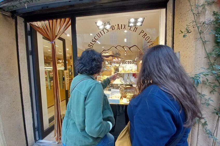Two people looking at a shop window with a sign that reads 'BISCUITS D'AIX EN PROVENCE.' 2