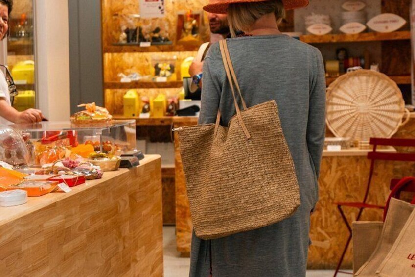 A person standing at a counter with a woven tote bag, in a store with wooden shelves and various items on display. 4