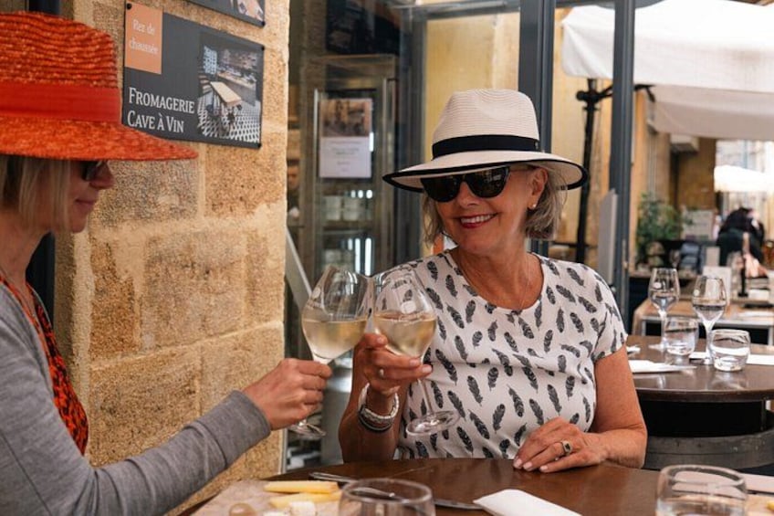 Deux personnes trinquent avec des verres de vin à une table dans un restaurant aux murs de pierre, où un panneau indique la présence d’une cave à vin. 2