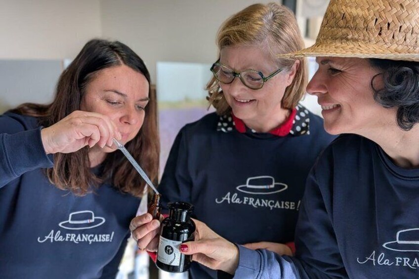 Three people wearing matching 'Ala Francaise!' aprons, one holding a bottle. 1
