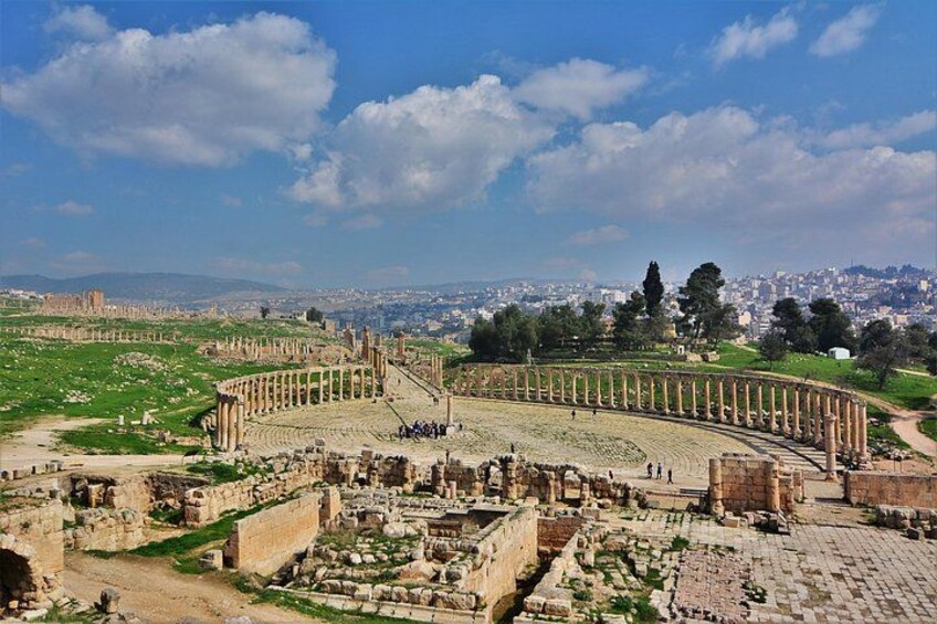 Ancient ruins with columns, a large amphitheater, and a cityscape in the background. 2