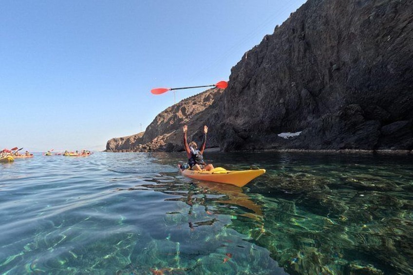 A kayaker in a yellow kayak on clear water with a rocky cliff in the background. 3