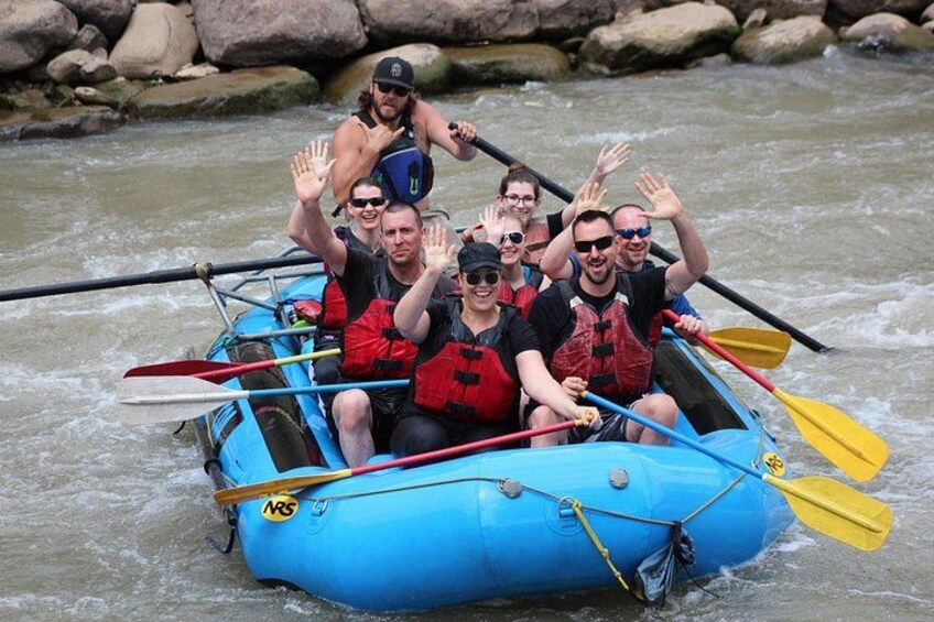 A group of people in a blue raft on a river, wearing life jackets and paddling with oars. 4