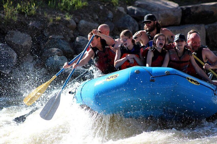 A group of people in a blue raft navigating through a river with rapids. 5