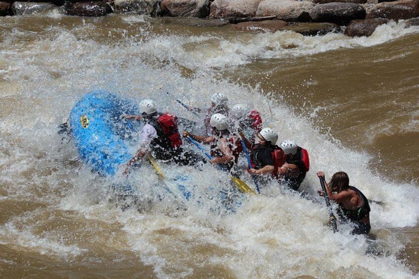 A group of people in a blue raft navigating through a river with rapids. 2