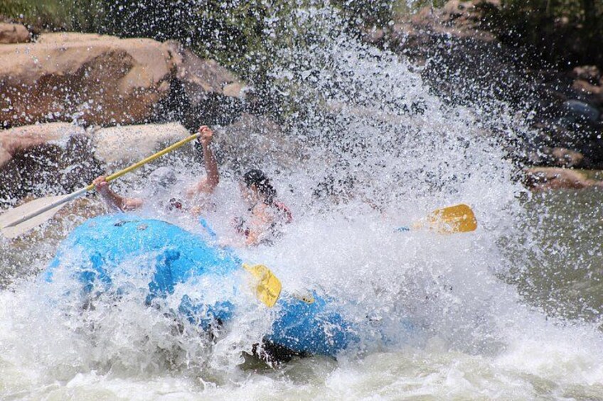 A person in a blue raft being propelled by a paddle through a body of water with splashes. 3