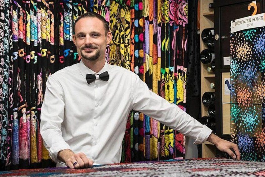 A person in a white shirt with a black bow tie standing in front of a display of colorful scarves. 5