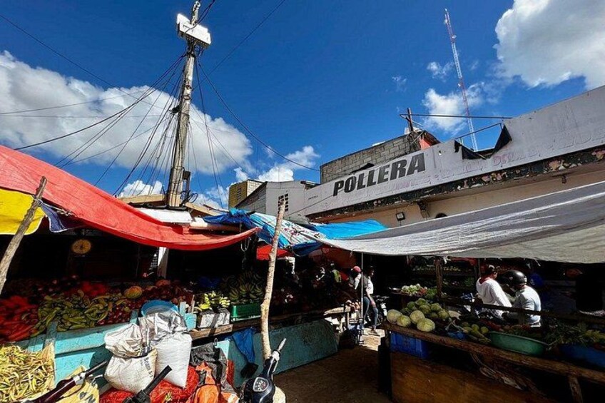 A bustling outdoor market with colorful canopies, a variety of fresh produce, and a building labeled 'POLLERA' in the background. 4