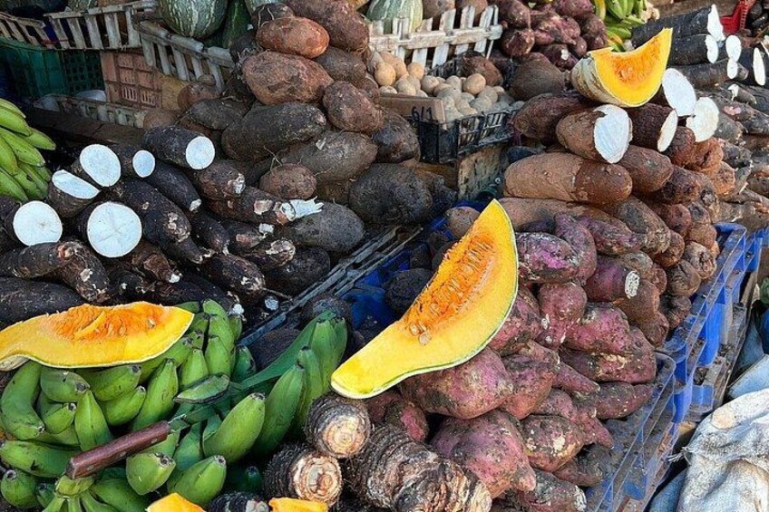 A market with various fruits and vegetables, including bananas, sweet potatoes, and a pumpkin. 5