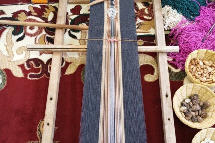 A loom with colorful threads and a patterned carpet in the background. 3