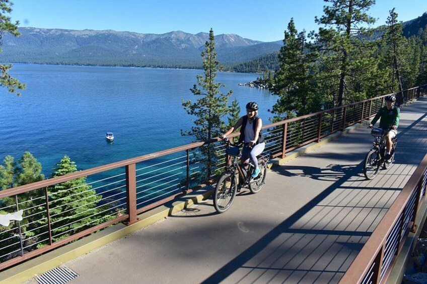 Two cyclists on a wooden bridge over a lake with mountains in the background. 4