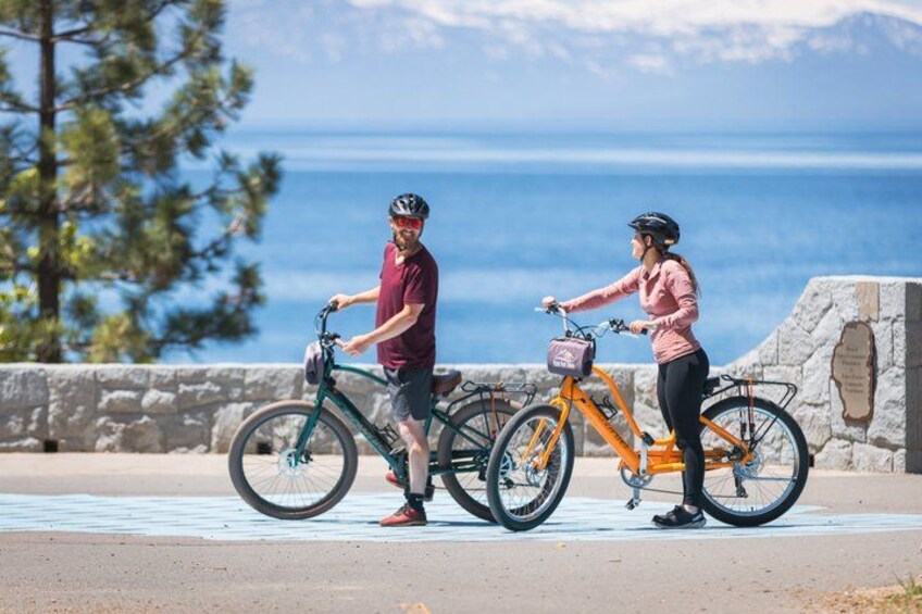 Two people on bicycles, a stone wall, and a body of water in the background. 2