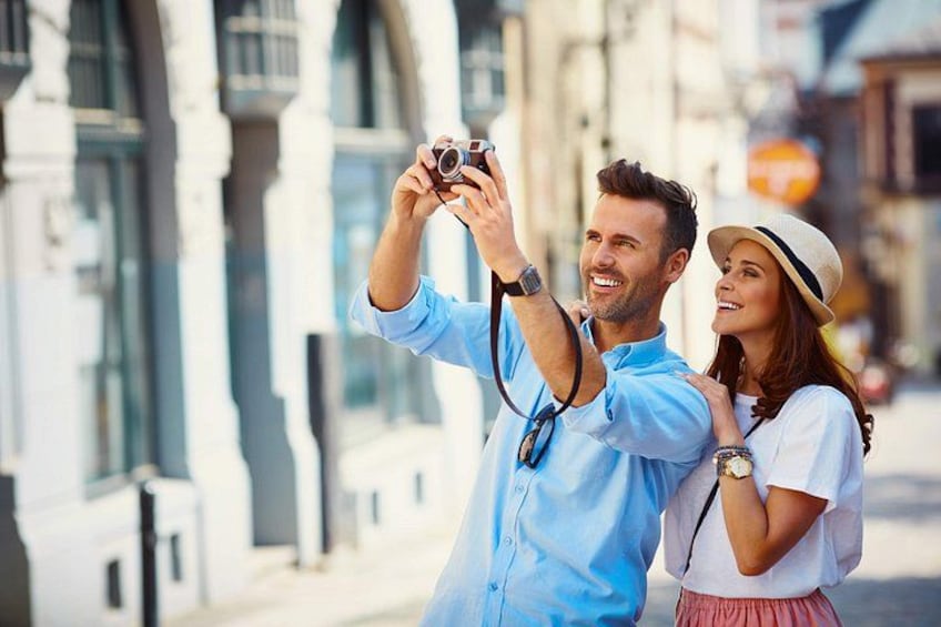 Un couple prend un autoportrait avec un appareil photo, debout devant un bâtiment doté de fenêtres en arc de cercle. 3