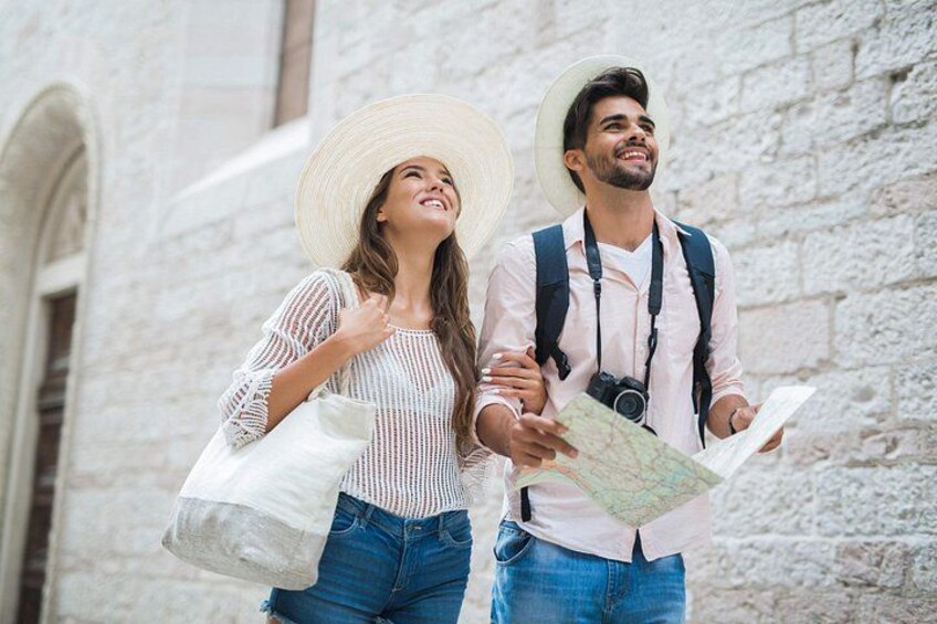 Due persone che camminano, una con una mappa in mano, di fronte a un edificio in pietra con finestre ad arco. 1