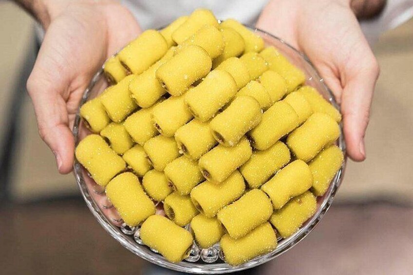 Une personne tenant un bol rempli de petites douceurs cylindriques, de couleur jaune et enrobées de sucre. 2