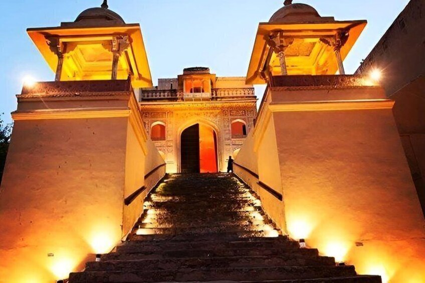 A grand entrance with a central archway, flanked by two illuminated pavilions, leading to a building with a dome. 2