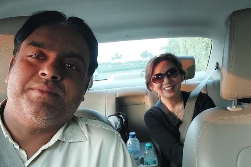 A man and a woman in a car with a seatbelt, a bottle of water, and a window showing greenery outside. 3