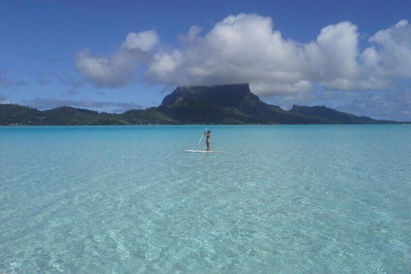 Una persona haciendo paddleboard en aguas turquesas cristalinas con una montaña al fondo. 5