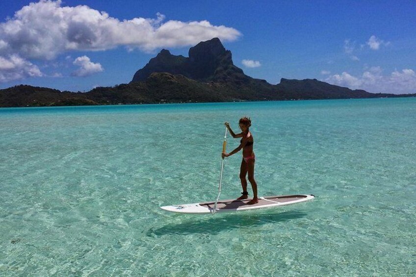 Una persona haciendo paddleboard sobre aguas turquesas cristalinas con un paisaje montañoso al fondo. 4