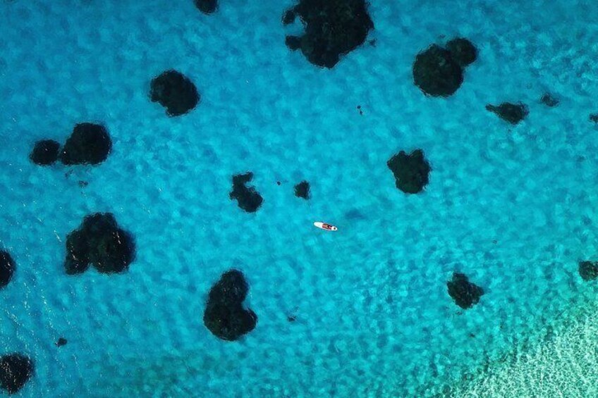 Mar azul transparente con rocas negras dispersas y un barco pequeño. 3
