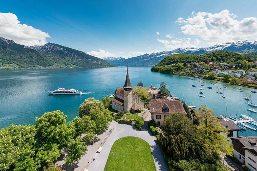 A lake with boats, a church, and mountains in the background. 1