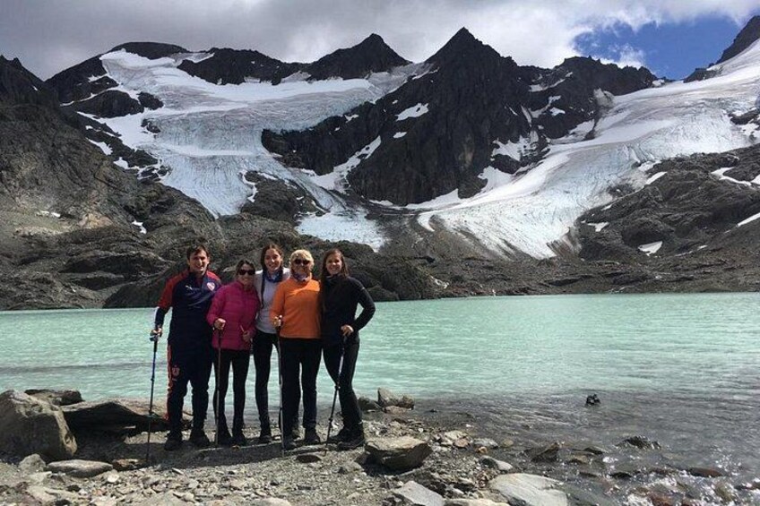 A group of people standing by a turquoise lake with snow-capped mountains in the background. 2