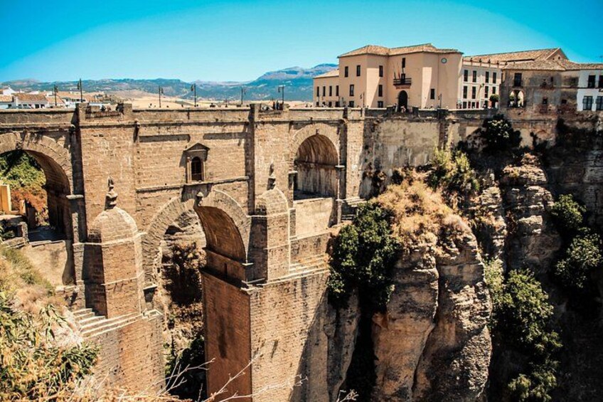 A stone bridge with arches, a building with a flat roof, and rocky cliffs. 1