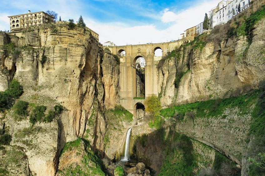 A stone bridge, a waterfall, and buildings on a cliff. 5
