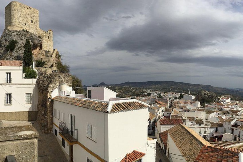 A coastal town with a historic stone tower, terracotta-roofed buildings, and a mountainous backdrop. 3