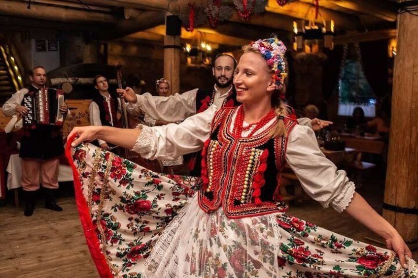 Una persona in abiti tradizionali che danza con un gruppo in un ambiente rustico. 2