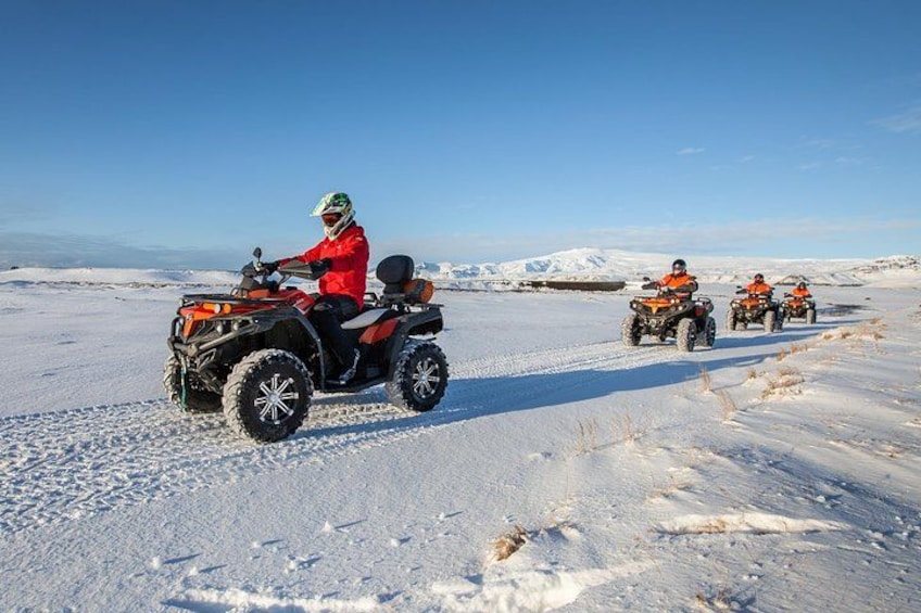 A person riding an ATV on a snowy landscape with mountains in the background. 2