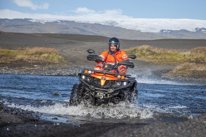 A person riding an ATV on a river surrounded by mountains. 4