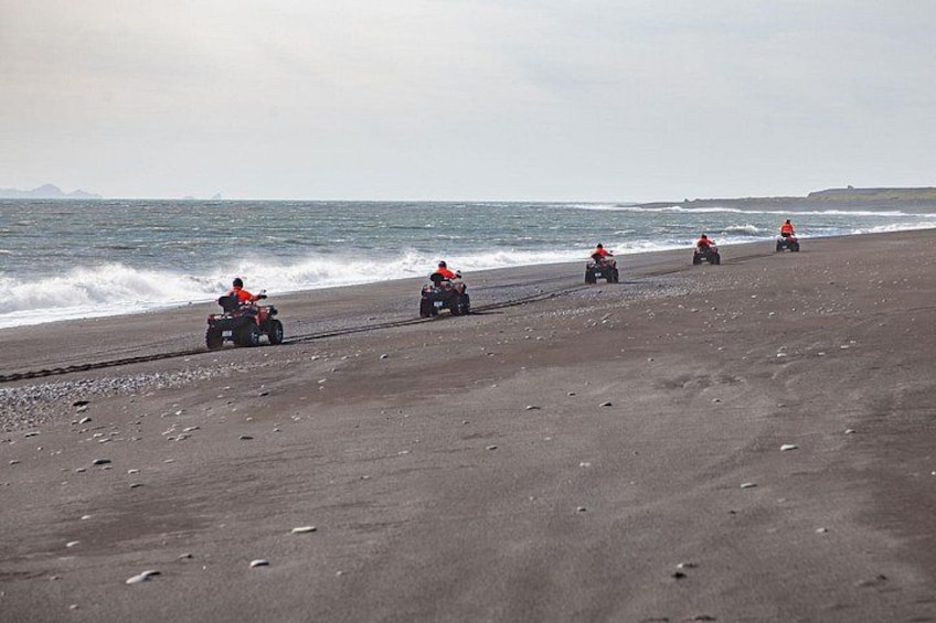 Four people on quad bikes on a sandy beach with the ocean in the background. 3