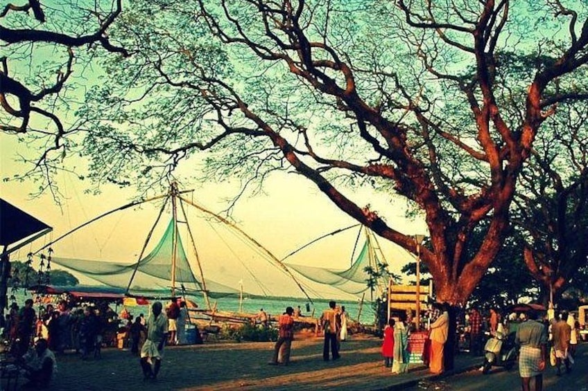 A market scene with people, a large tree, and a tent structure. 1