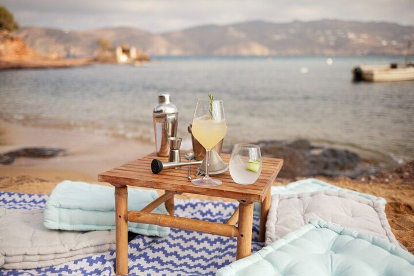 Een houten tafel met een cocktail, een shaker en een glas op een strand, met een deken en kussens. 5