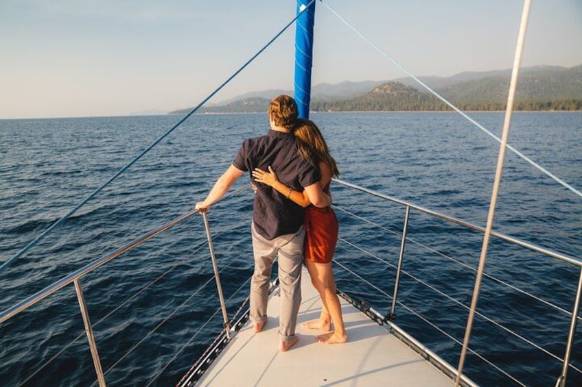 Una pareja en un velero con vistas al mar y montañas a lo lejos. 3