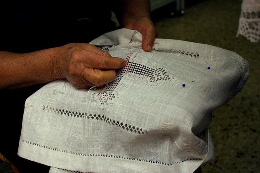 Hands working on a white fabric with lace patterns and blue pins. 2