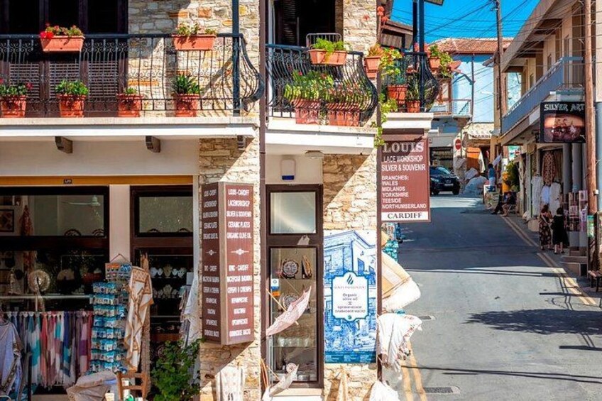 Una calle estrecha con tiendas, un letrero que dice 'Louis Lace Workshop' y balcones con plantas. 3